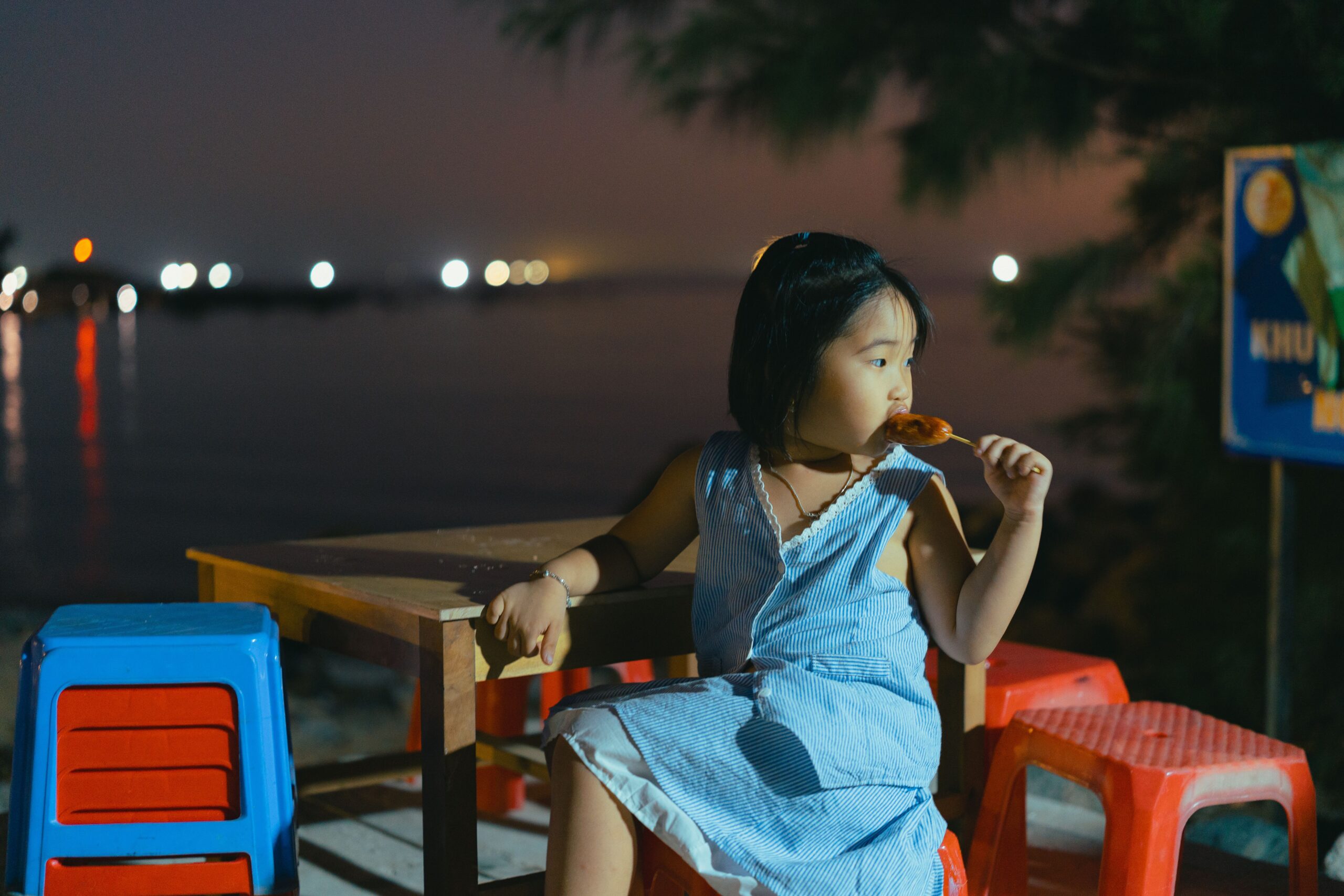 Young girl enjoying a grilled skewer on an evening family food tour in Da Nang